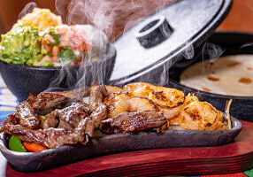 Steak and Shrimp Fajitas with sides, steam rising and tortillas in background