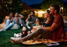 Happy,Couple,Watching,Movie,With,Friends,In,The,Backyard,At