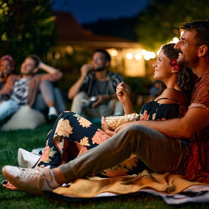 Happy,Couple,Watching,Movie,With,Friends,In,The,Backyard,At